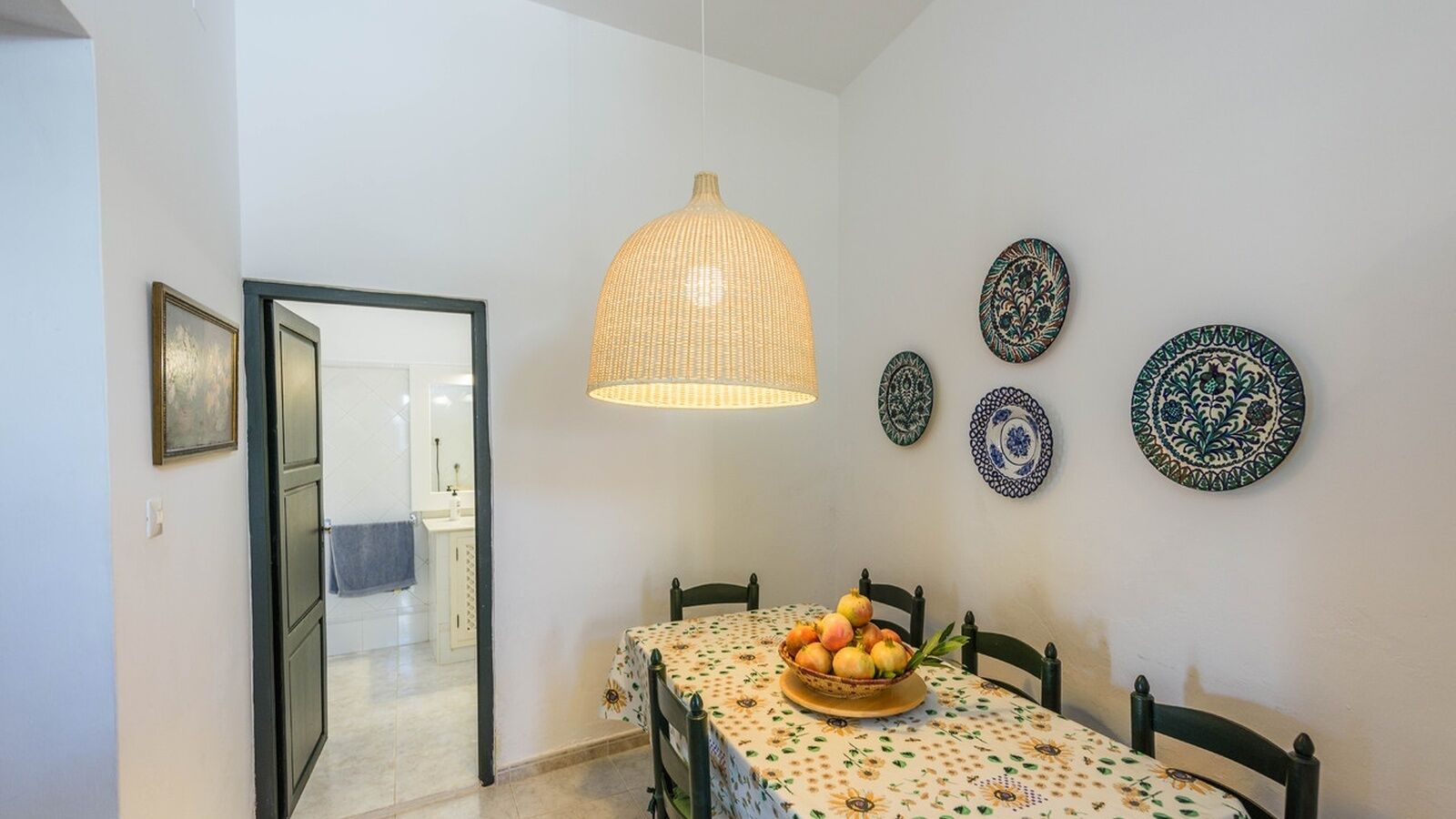 Un coin repas avec une table dressée pour quatre personnes, un luminaire suspendu et des assiettes décoratives accrochées au mur.