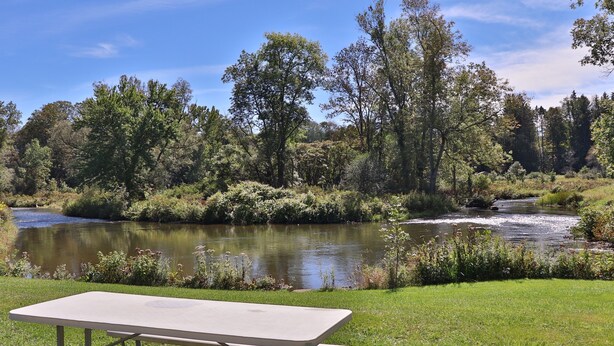 Una mesa de picnic en un área con césped, con un río y árboles al fondo.