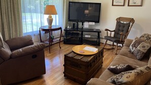 Una sala de estar con sofá, sillón, mesa de centro de madera y televisor sobre un mueble.
