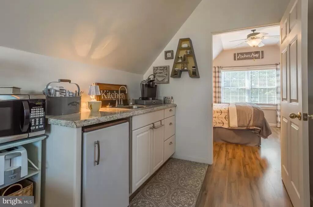 A compact kitchen with a microwave, coffee maker, and a 'Kitchen' sign. A bed is visible in the adjacent room.