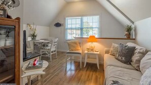 Un espai d'estar acollidor d'estil loft amb zona de menjador, un sofà amb coixí que diu 'Love This Place' i una finestra amb persianes.