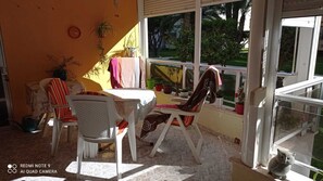 Un patio iluminado por el sol con una mesa y sillas, plantas en macetas y vistas al verdor exterior.