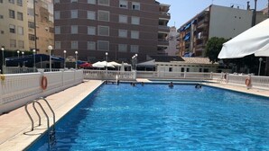 A swimming pool with clear blue water, surrounded by a white fence and a white umbrella. - Apartment in Eliteresidenz El Palmeral in Torrevieja (Torrevieja)