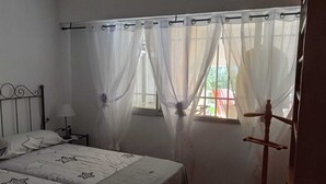 A bedroom with a bed, a nightstand, a window with sheer curtains, and a wooden chair. - Apartment in Eliteresidenz El Palmeral in Torrevieja (Torrevieja)