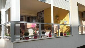 A balcony with a glass railing, potted plants, and a view of a yellow building. - Apartment in Eliteresidenz El Palmeral in Torrevieja (Torrevieja)