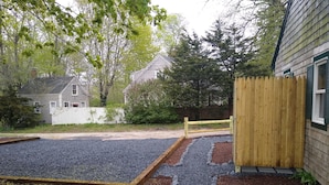 Een grindpad leidt naar een houten hek, met een huis en een wit schutting op de achtergrond.