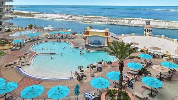Ein Resort mit großem Pool, Liegestühlen, Sonnenschirmen und Blick auf Strand und Meer.