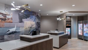 Ein moderner Empfangsbereich mit einer großen Wandmalerei zum Thema Weltraumforschung, einem Holzbüro, einer Theke und einem mit Getränken gefüllten Kühlschrank.