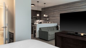 Ein modernes Hotelzimmer mit einem großen Bett, einem Fernseher, einer Sitzecke und einer Küchenzeile.