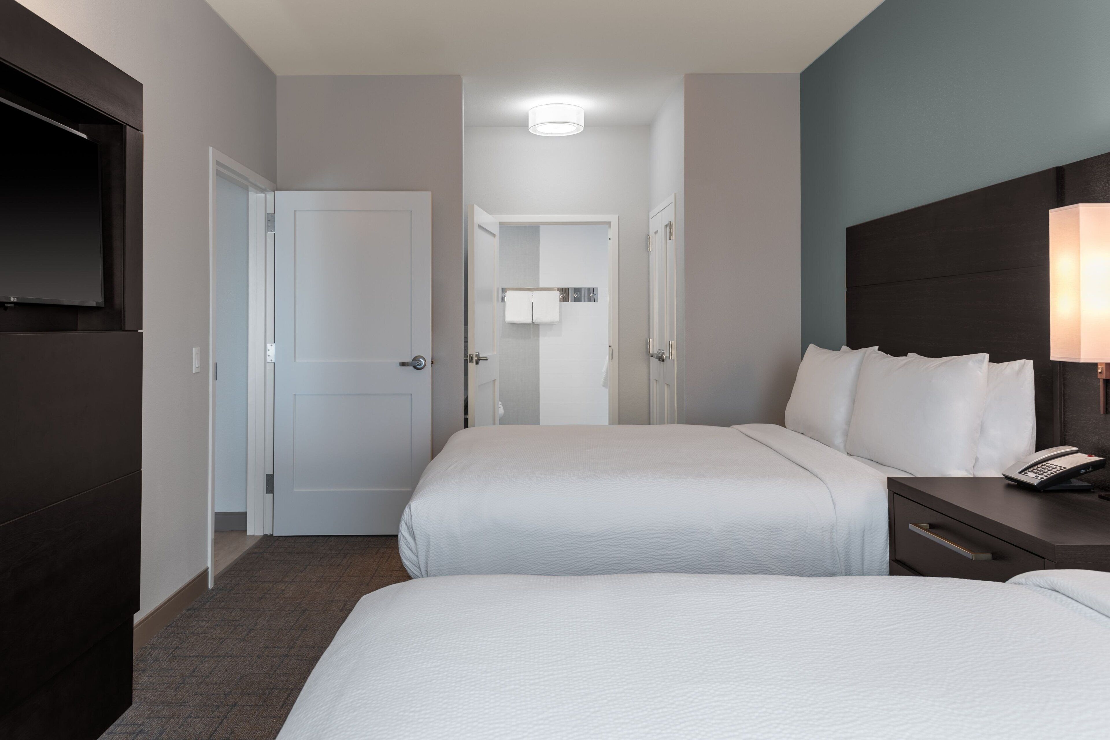 A hotel room with two beds, a TV, a bedside lamp, and a bathroom visible through an open door.