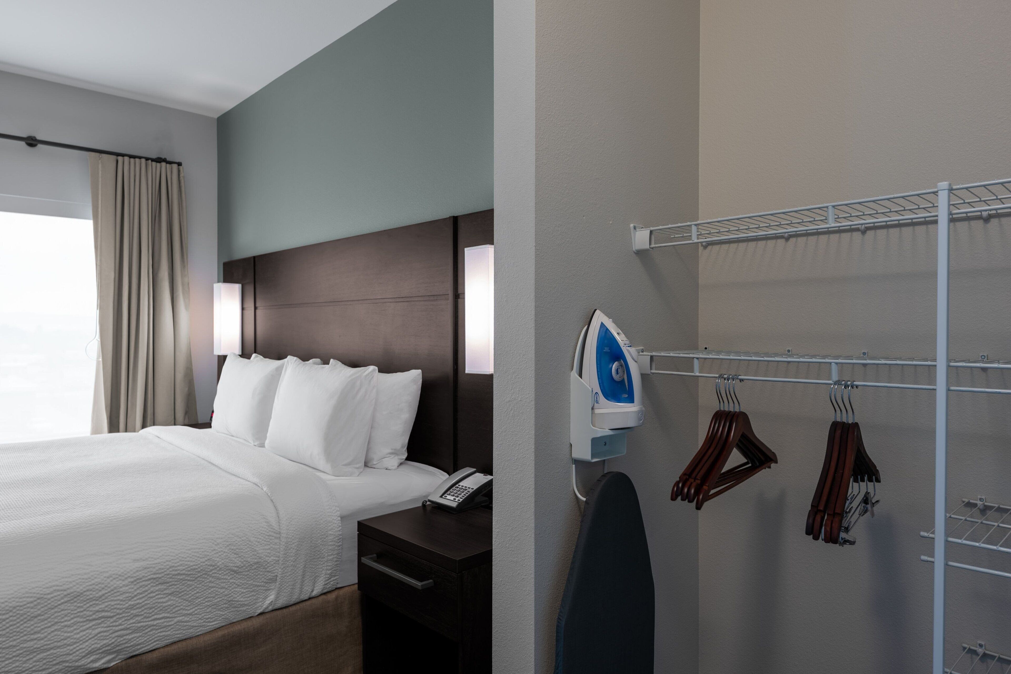 A hotel room with a bed, bedside table, and a wall-mounted ironing board with hangers.
