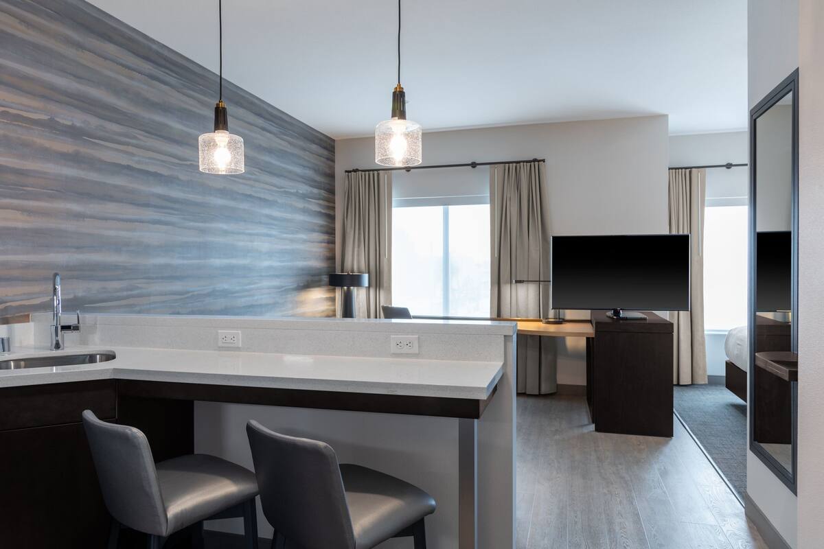 A modern hotel room with a kitchen area, a large flat-screen TV, and a large mirror.