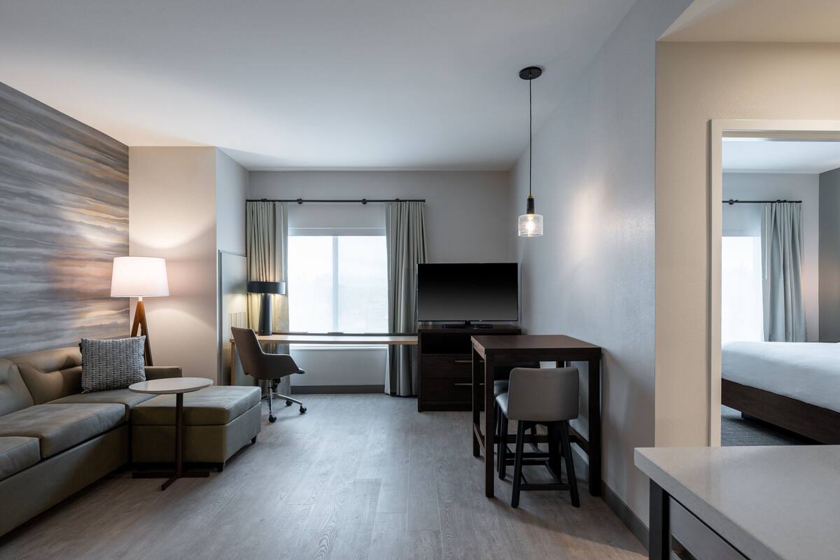 A modern hotel room with a sofa, a small table, a desk, a TV, and a bed.