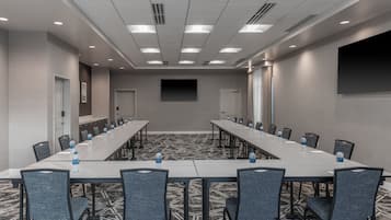 Un salón de conferencias con una larga mesa, sillas, botellas de agua y una pantalla de proyector.