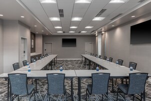 Un salón de conferencias con una larga mesa, sillas, botellas de agua y una pantalla de proyector.