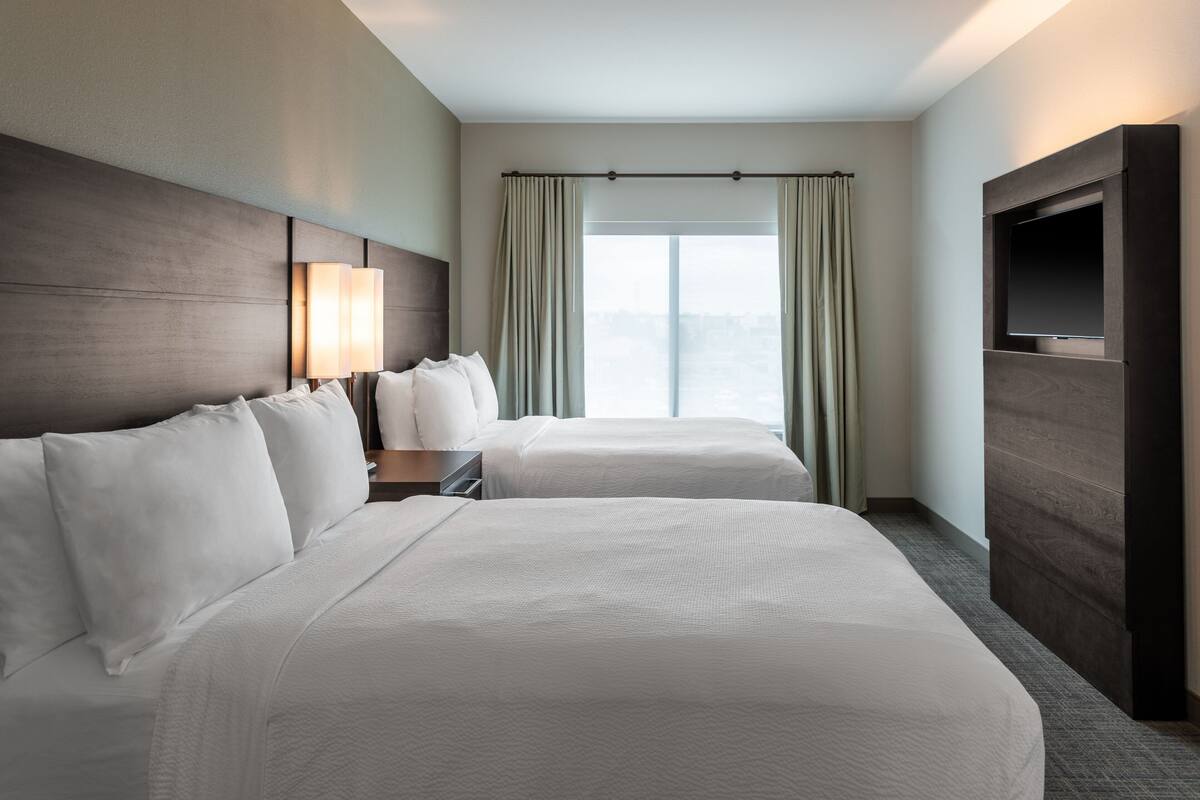 A hotel room with two beds, a TV, a window with curtains, and a city view.