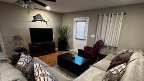 Ein Wohnzimmer mit Ecksofa, Flachbildfernseher, Deckenventilator und Topfpflanze.