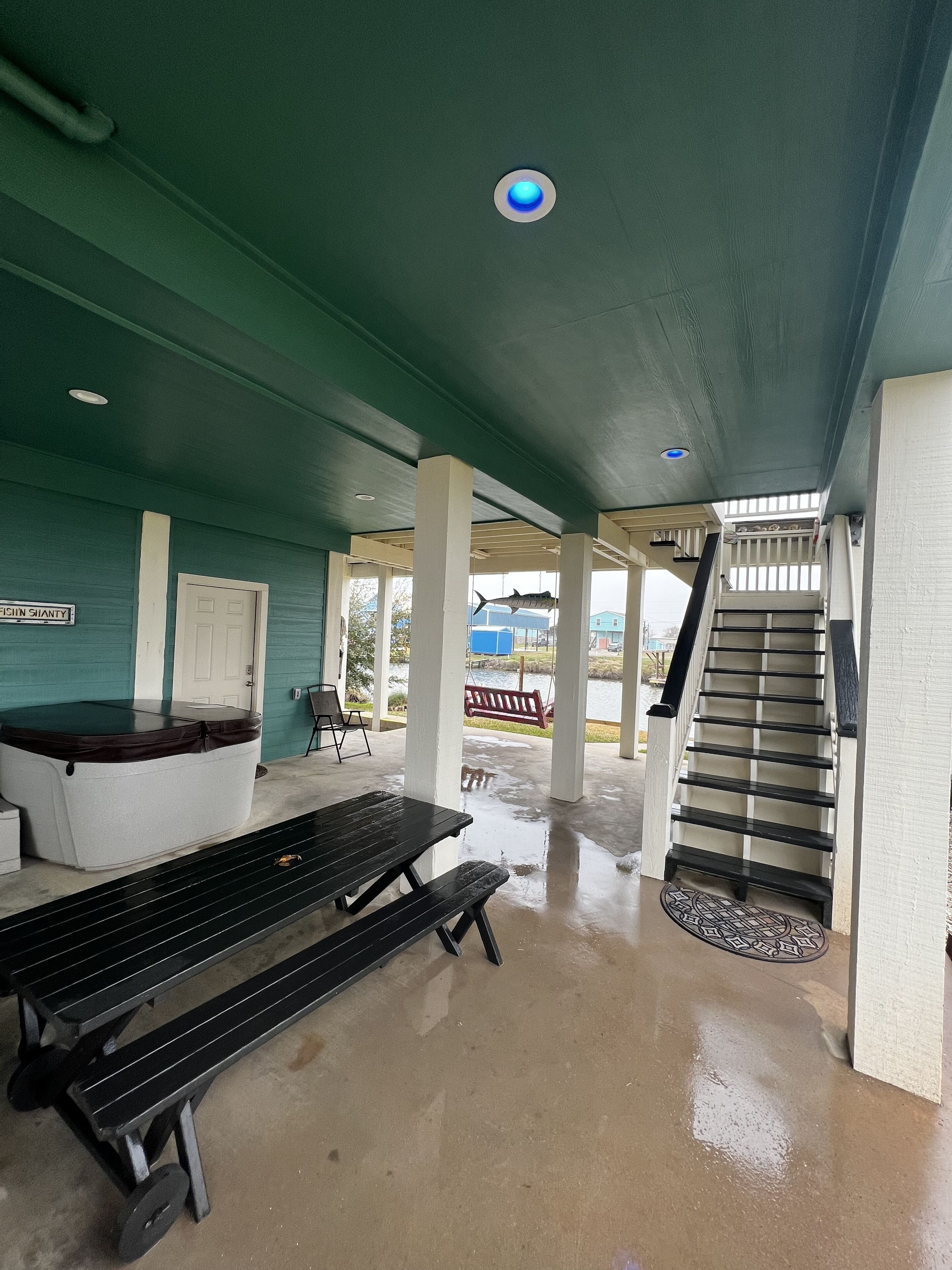 A covered outdoor area with a hot tub, benches, and a staircase leading to an upper level.