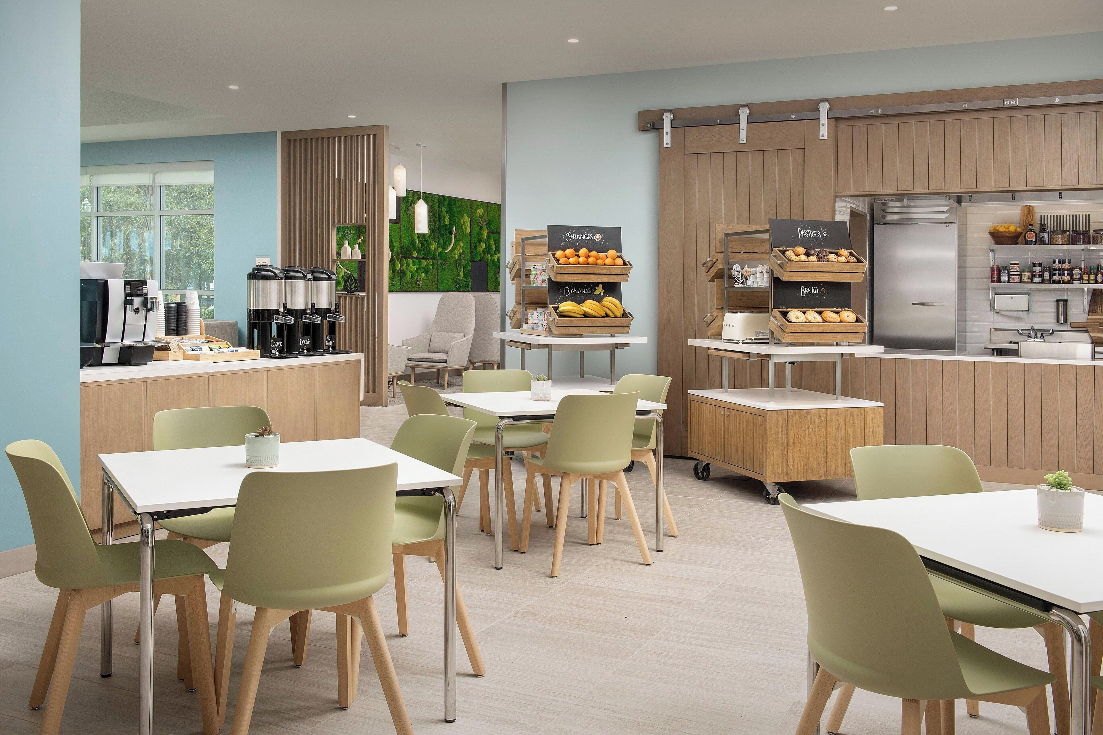 A modern kitchen with a coffee station, fruit display, and a refrigerator.