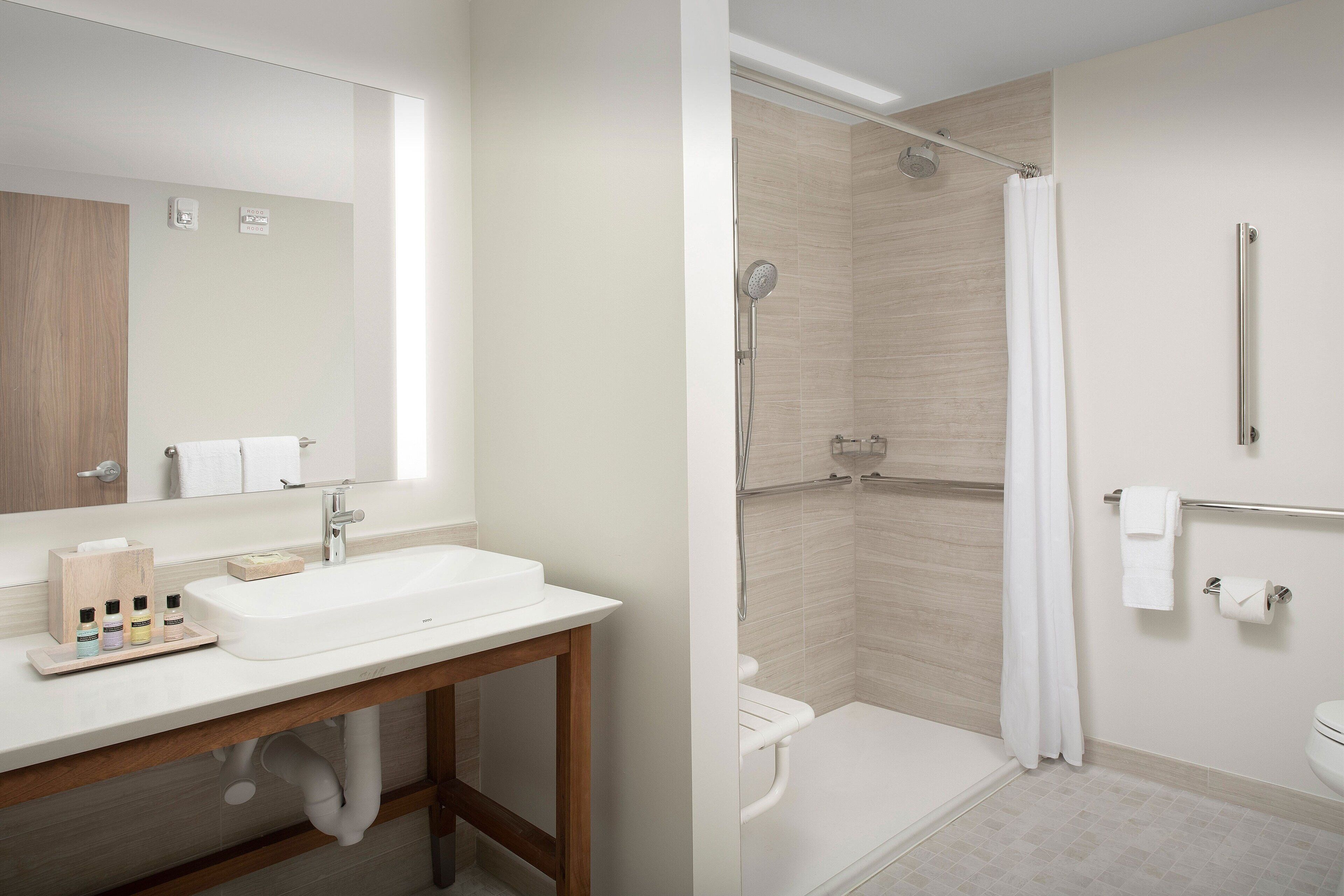 A modern bathroom with a sink, mirror, shower, and toilet.