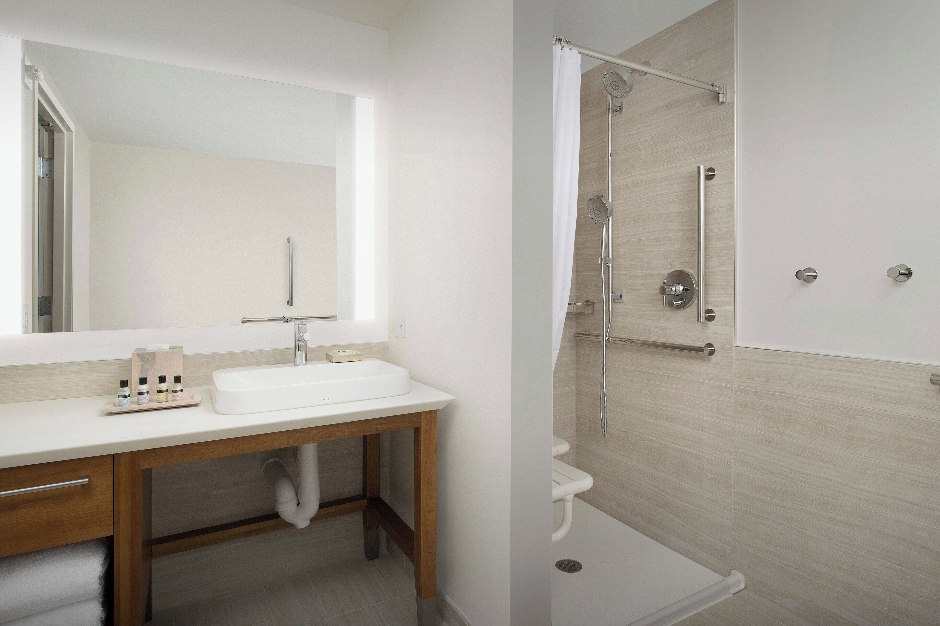 A modern bathroom with a white sink, wooden vanity, and a shower with a glass door.