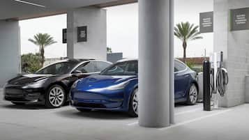 A modern electric vehicle charging station with two cars parked nearby.