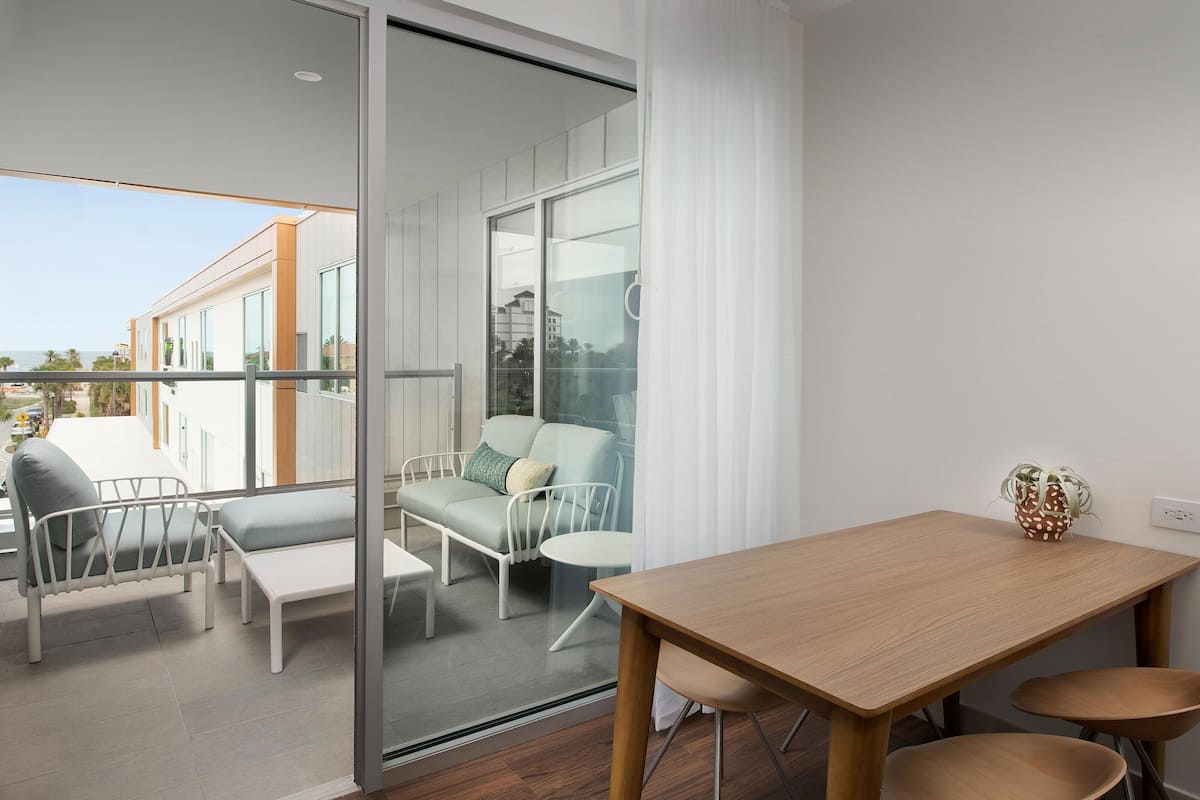 A modern balcony with a glass door, a wooden table, and two chairs.