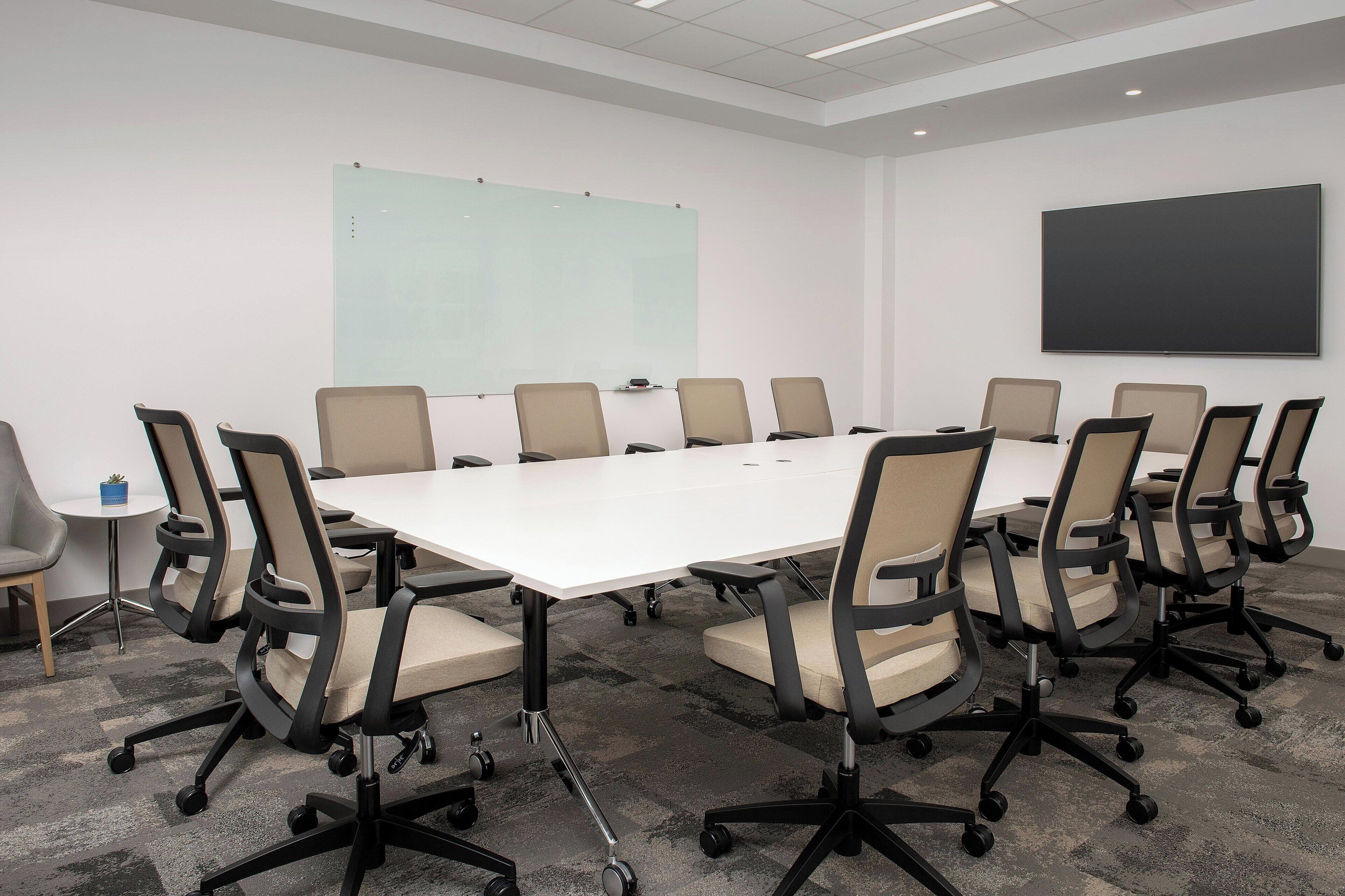 Une salle de conférence équipée d’une grande table, de plusieurs chaises, d’un tableau blanc et d’un écran de projection.