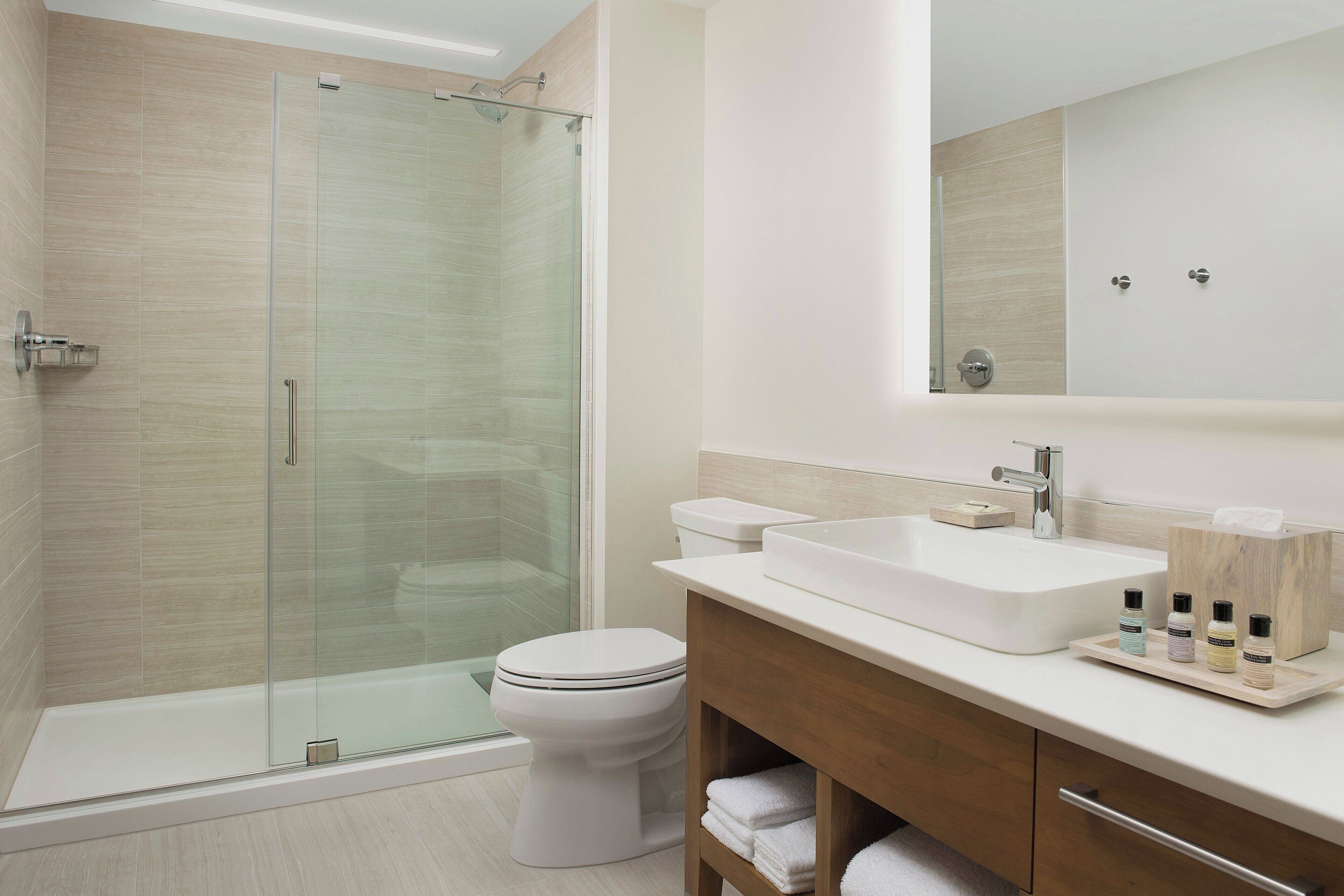 A modern bathroom with a glass-enclosed shower, a white toilet, and a wooden vanity with a large sink and toiletries.