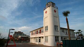 A building with a red cross symbol, indicating it is a medical facility, with a clear sky and palm trees in the background.