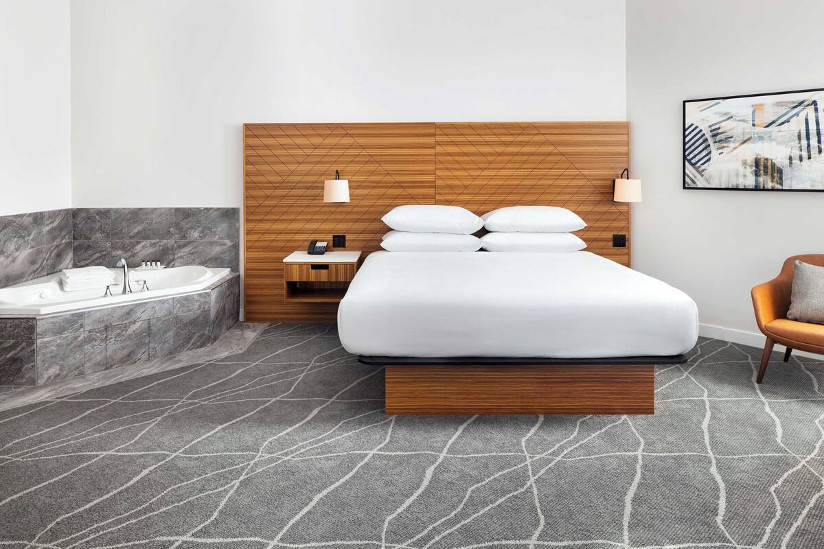 Une chambre d’hôtel moderne avec une tête de lit en bois, un grand lit, une baignoire et une chaise.