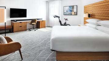 A modern hotel room with a large bed, a desk with a chair, a television, and a bicycle.