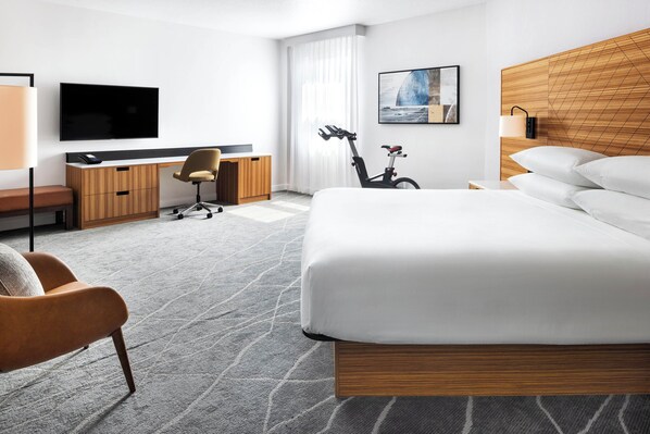 A modern hotel room with a large bed, a desk with a chair, a television, and a bicycle.