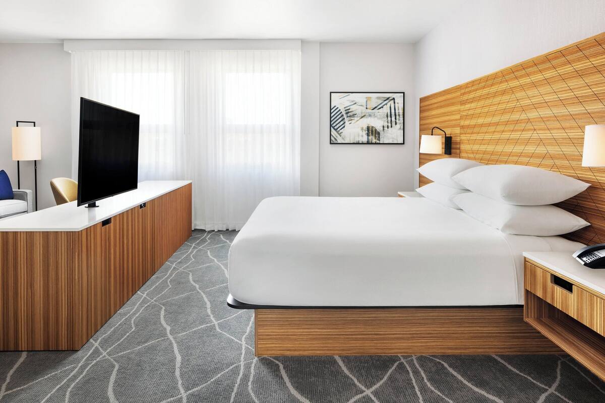 Une chambre d’hôtel moderne dotée d’un grand lit, d’un bureau, d’une télévision à écran plat et d’une œuvre d’art accrochée au mur.