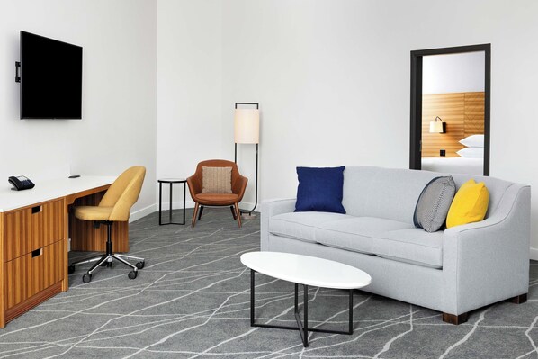 A modern hotel room with a desk, office chair, sofa, and a small table.