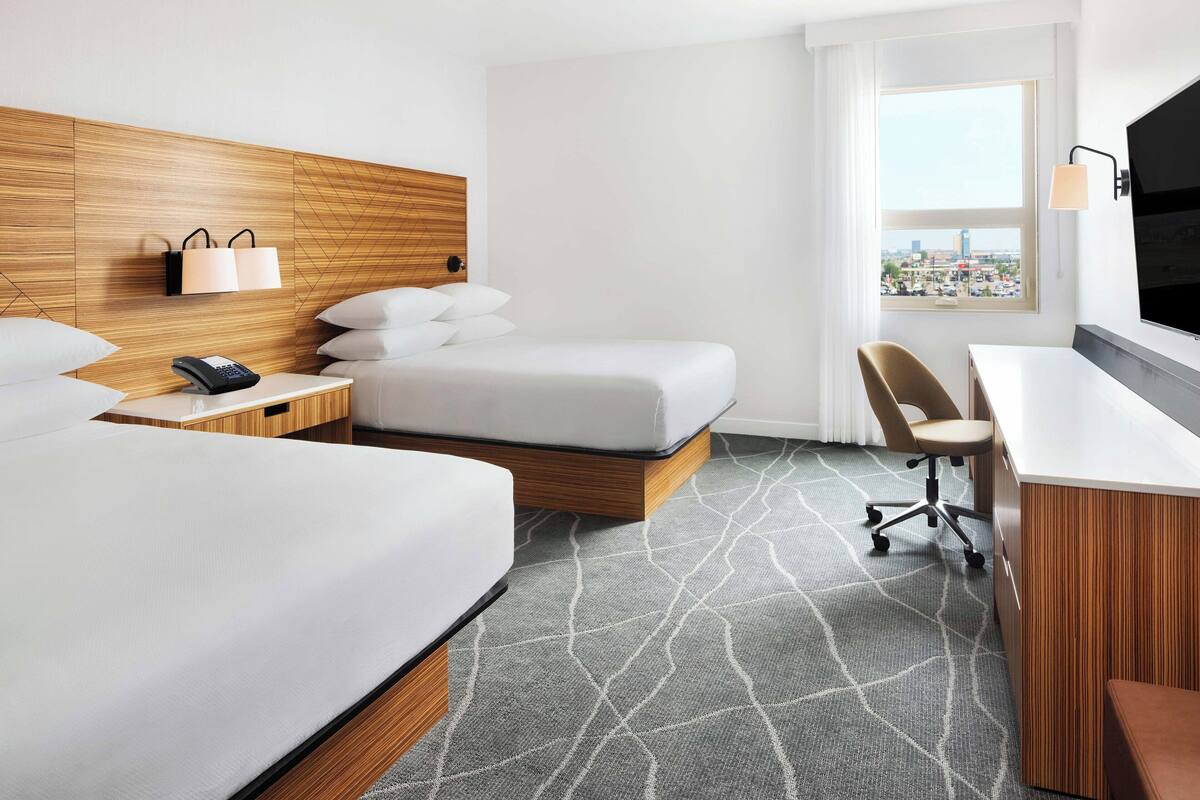Une chambre d’hôtel avec un grand lit, un bureau, une chaise, une télévision et une fenêtre donnant sur la ville.