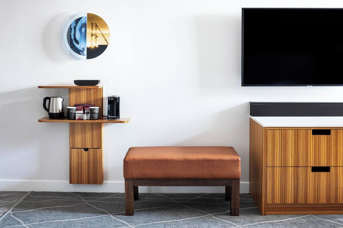 Un salon moderne avec un banc en bois, un téléviseur fixé au mur et une petite étagère contenant des ustensiles de cuisine.