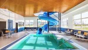 Una piscina interior con tobogán azul, zonas de estar y ventanas amplias.