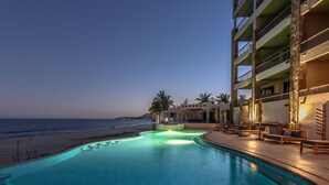 Ein Pool mit geschwungener Form, Blick auf den Strand und ein Gebäude mit Balkonen und Außenbereich.