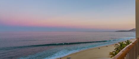Vista de una playa con barandilla de madera, mar tranquilo y cielo despejado.