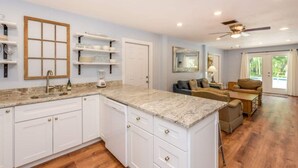 A spacious kitchen with white cabinets, a granite countertop, and a ceiling fan. - Main-Stay is a larger 2/1 central to all Naples (Naples)