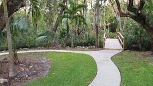 A pathway leading to a wooden bridge in a lush garden with palm trees and dense foliage. - Main-Stay is a larger 2/1 central to all Naples (Naples)