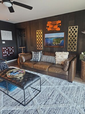 A living room with a brown leather sofa, a black ottoman, and a patterned rug.