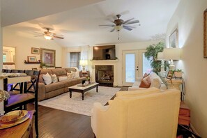 A living room with a fireplace, a ceiling fan, and a dining area with a table and chairs. - Family-Friendly Home w/ Lake Oconee Access + Patio (Eatonton)