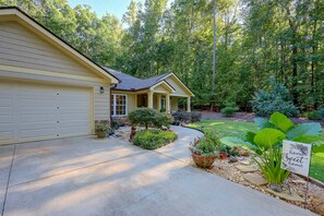 A residential house with a garage, a covered porch, and a well-maintained garden with various plants and a sign that reads 'home Sweet home'. - Family-Friendly Home w/ Lake Oconee Access + Patio (Eatonton)