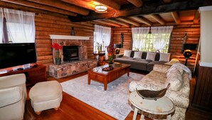 Interior de una cabaña de troncos con chimenea, sofá, televisor y piso de madera.