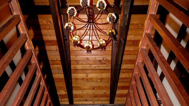 Una escalera de madera con candelabro, barandillas de madera y un ventanal con una planta.
