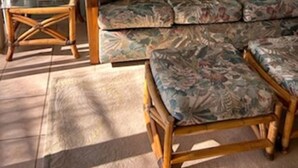 Ein Wohnzimmer mit einem blumigen Sofa, einem passenden Sessel, einem kleinen Holztisch mit Lampe und einem Spiegel an der Wand.