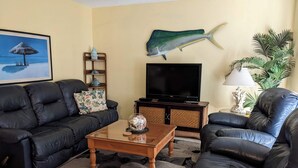 A living room with a sofa, a coffee table, a TV, and a decorative fish on the wall. - COCOA BEACH OASIS, STEPS TO THE BEACH, HEATED POOL, GREAT AMENITIES AND LOCATION (Cocoa Beach)