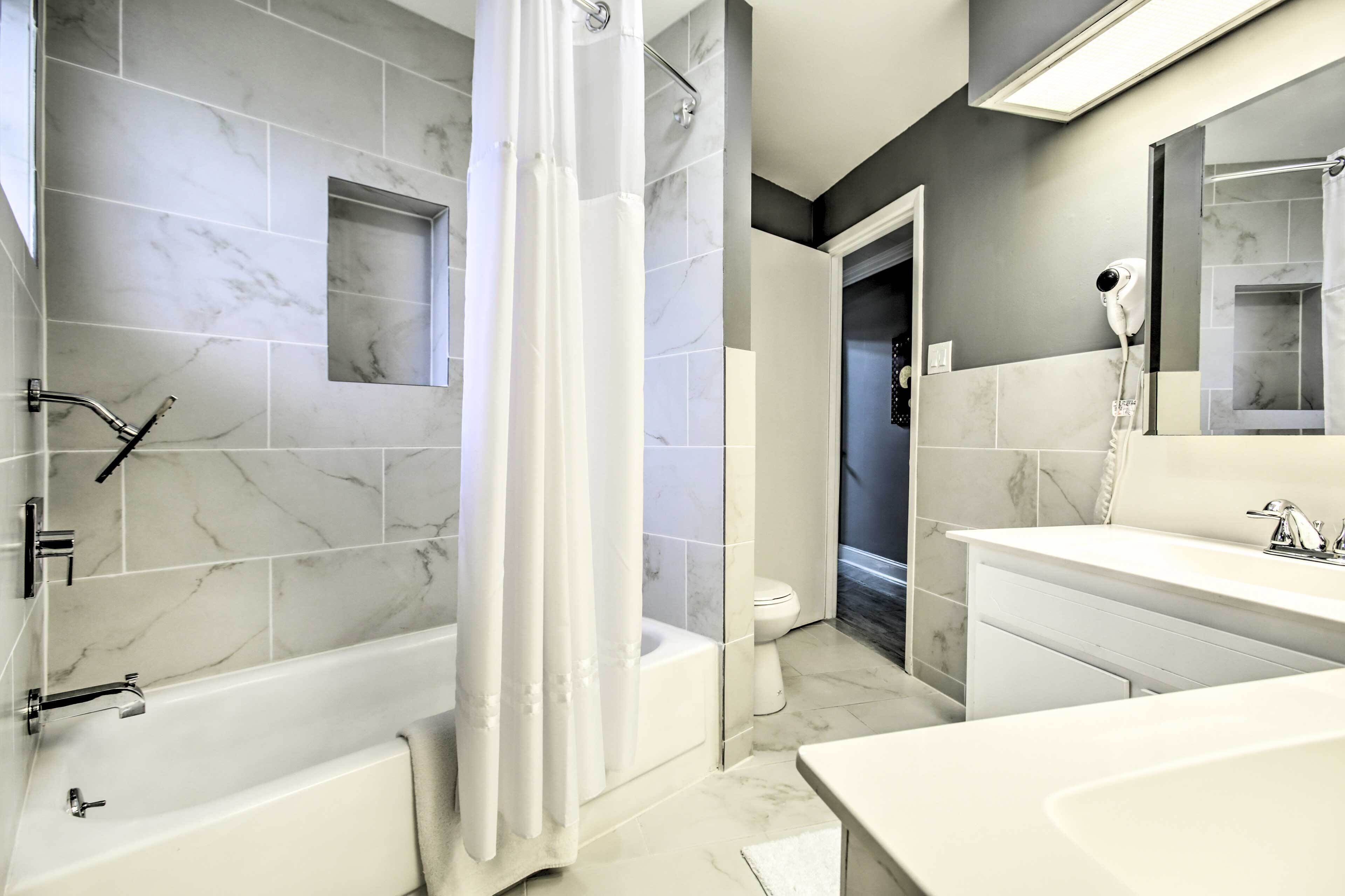 Ein modernes Badezimmer mit Badewanne, Dusche und Toilette, ausgestattet mit Marmorfliesen und einem großen Spiegel.